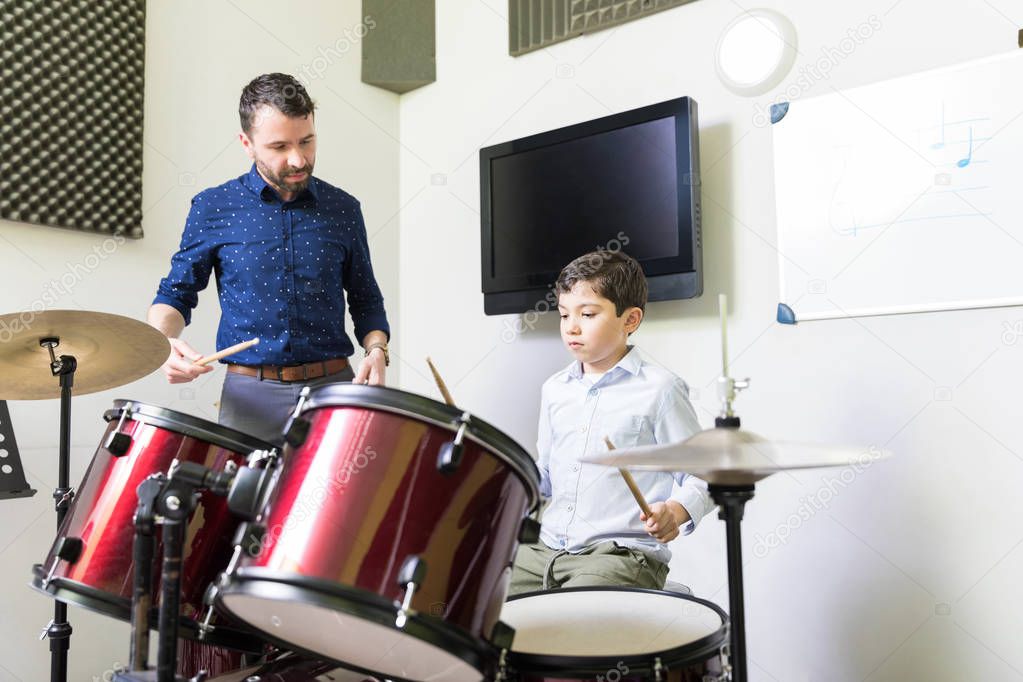 Male teacher guiding little boy in drum learning tutorial at music academy