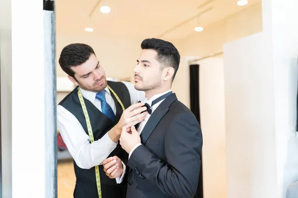 店員のスーツを借りるお店に立っているクライアントに蝶ネクタイを調整 — ストック写真