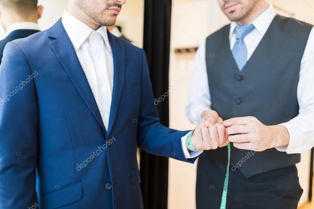 Midsection of creative young seamster measuring wrist of wealthy man in clothing store
