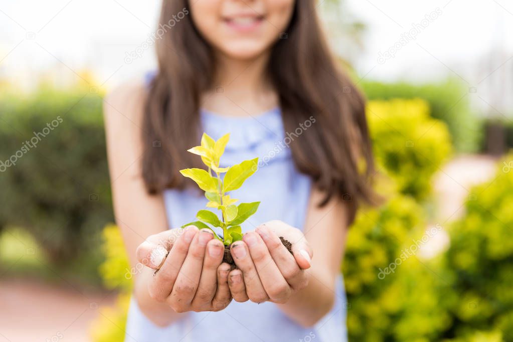 Hispanic girl protecting small plant on Earth Day in garden