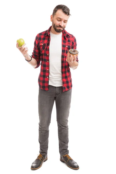 雄性嬉皮士忽略了一个苹果 并选择美味的甜甜圈 而站在白色的背景 — 图库照片