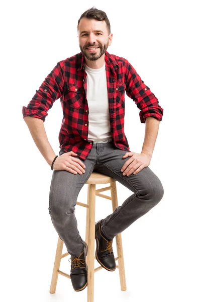 普通の背景に腰掛けに座っているスマートな男の全長 — ストック写真