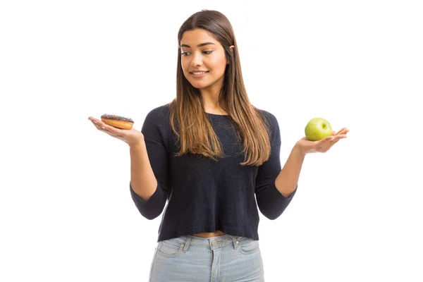 白い背景に立ちながら健康なリンゴと不健康なドーナツの間で決定する思慮深い女性 — ストック写真