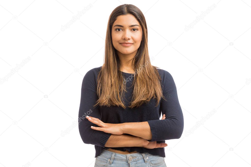 Portrait of good looking woman smiling while standing with arms crossed against plain background