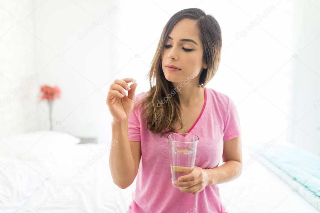 Sick mid adult woman taking dose of medicine while sitting on bed