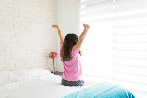 ベッドに座りながら手を伸ばしてエネルギーを高める女性の背面図 — ストック写真