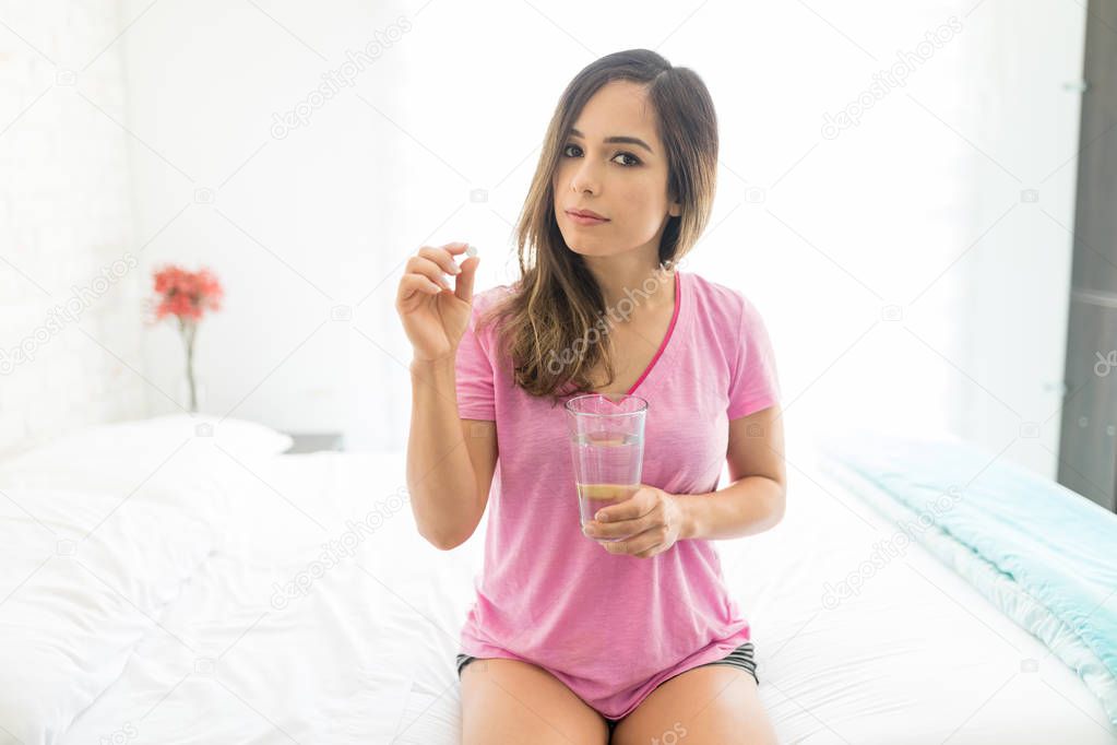 Portrait of woman taking tablet while suffering from bad health and relaxing on bed