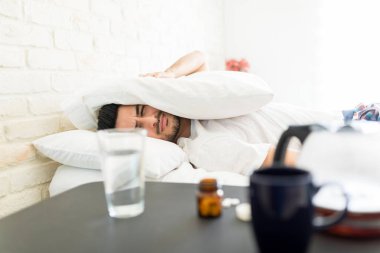 Yatak odasında yatarken hoş olmayan bir yüz yapma yastık ile kafa kapsayan sinirli adam