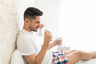 Üzgün Hispanic adam tutan tıp ve bardak su içinde yatak odası