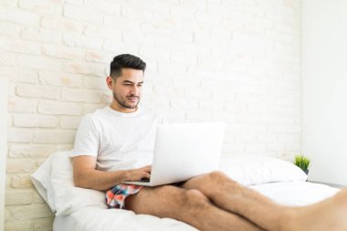 Yatak odasında otururken çekici İspanyol adam internet üzerinden bilgi arıyor