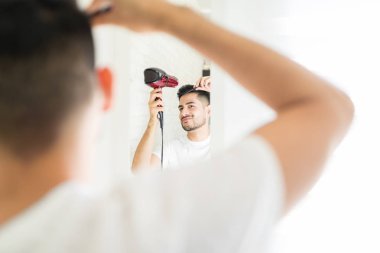 Hispanic iyi görünümlü adam saç kurutma makinesi ve fırça ile saç yapma