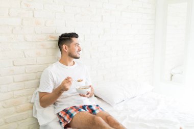 Yatakta mısır gevreği olan mutlu Latin adam