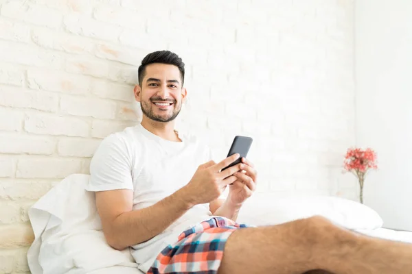 有魅力的男人在卧室里的智能手机上安装新的应用程序的肖像 — 图库照片