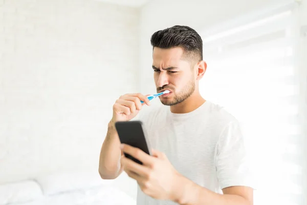 Giovane Uomo Lavarsi Denti Mentre Utilizza Smartphone Casa — Foto Stock