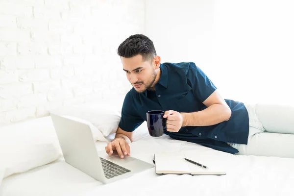 Sério Homem Atraente Segurando Xícara Café Usar Laptop Cama — Fotografia de Stock