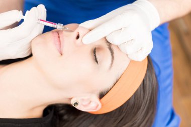 Cosmetic practitioner injects liquid into nose of patient to change the shape of nasal clipart
