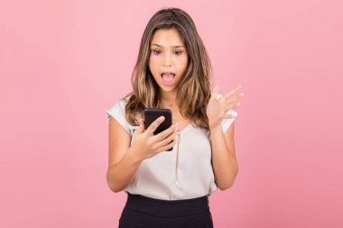 Pembe arka planda cep telefonundan ezici bir sürpriz mesaj okuyan kadın