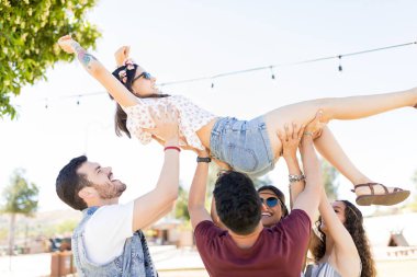 Müzik festivalinde genç kadını başlarının üstünde taşıyan neşeli arkadaşlar