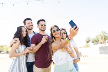 Müzik festivalinde akıllı telefon kullanarak arkadaşlarıyla selfie çeken güzel genç kadın