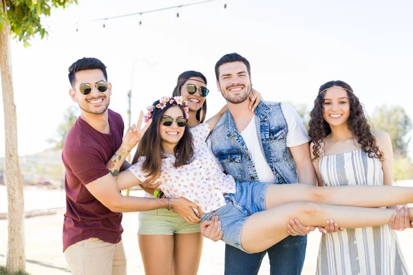 Happy best buddies lifting attractive woman gesturing peace sign at music festival