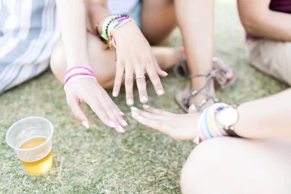 Cropped image of female friends matching painted nails while sitting on field during summer