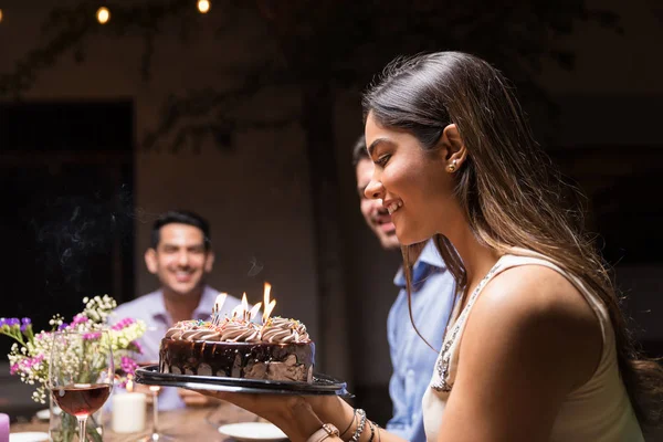 パーティーでキャンドルでバースデーケーキを見て笑顔の若い女性 — ストック写真