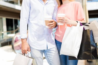 Alışveriş merkezinde tek kullanımlık kahve fincanları ve çantaile genç adam ve kadın Orta bölümü