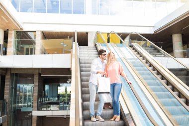 Alışveriş merkezinde yürüyen merdivendeki genç beyaz çift.