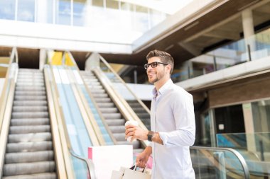 Tek kullanımlık kahve fincanı ve alışveriş merkezinde dolaşan çantaile trendy adam