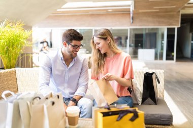 Kafede otururken kadın tarafından tutulan alışveriş çantasının içine bakan mutlu adam