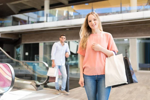 有吸引力的年轻女子拿着购物袋与男友在商场的背景肖像 — 图库照片