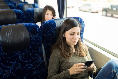 Otobüste seyahat ederken akıllı telefondan müzik dinleyen esmer yolcu