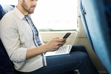 Otobüste seyahat ederken cep telefonu ve dizüstü bilgisayar kullanan yolcu