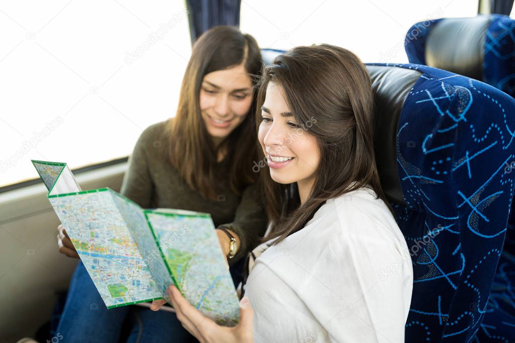 Latin female friends exploring map while traveling in tourist bus