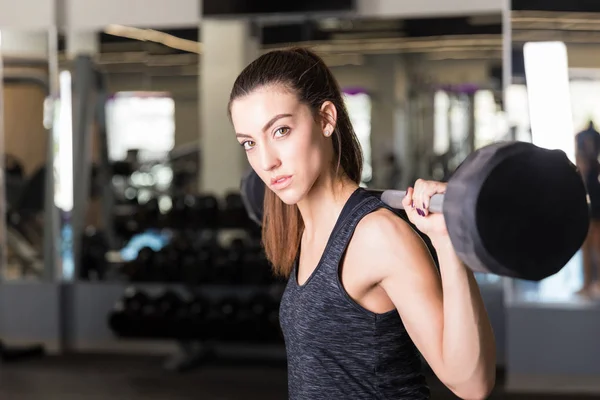 Powerful young woman lifting barbell during cross-training workout at gymnasium