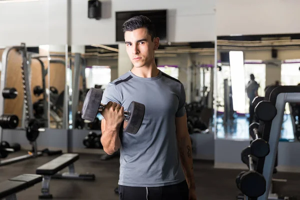 Motivated young man is working hard to stay in shape while standing in gym