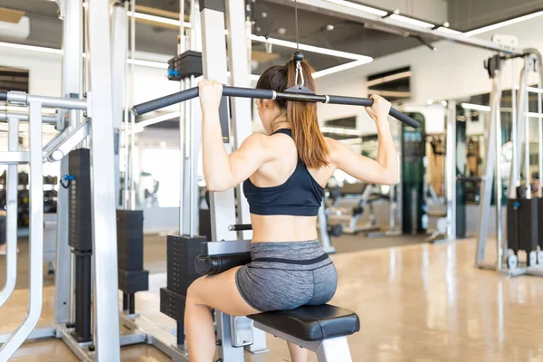 Young woman improving posture and spine health with pulldown exercise in gym