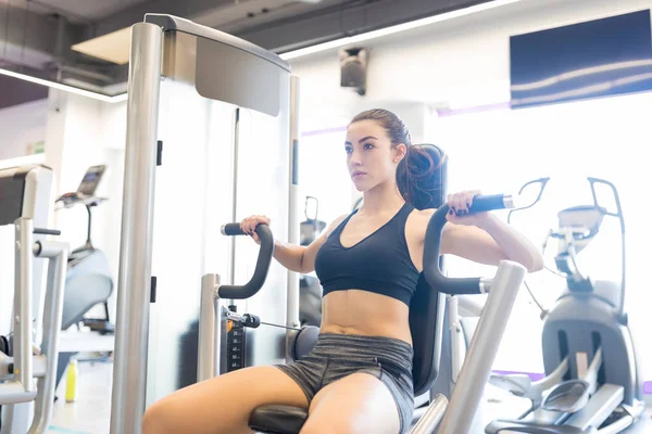 Active woman in sportsbra using chest-press machine to workout in gym