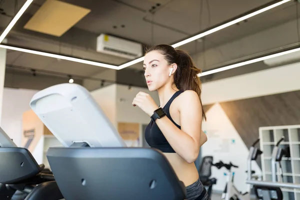 坚定的年轻女子听音乐 而在健身房的跑步机上锻炼 — 图库照片