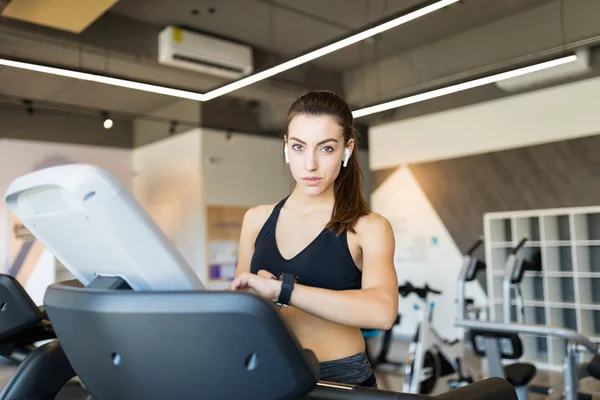 在健身房的跑步机上使用智能手表的专用女性的肖像 — 图库照片