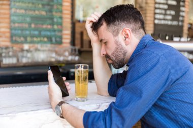 Bar tezgahında bira içerken akıllı telefon kullanan depresif adam