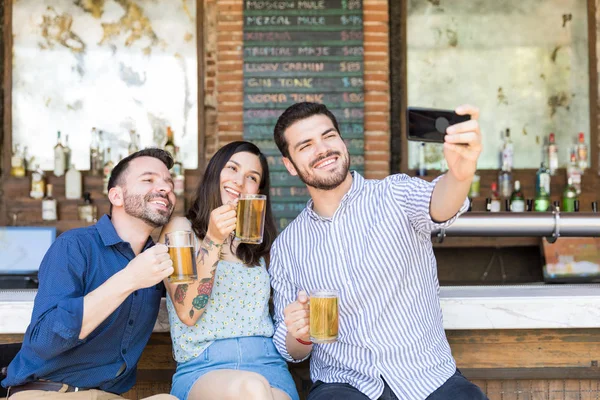 レストランでスマートフォンでビールグラスで自分撮りをする幸せな友人 — ストック写真