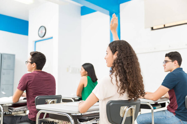 Teenage girl with raised hand asking question in class at school