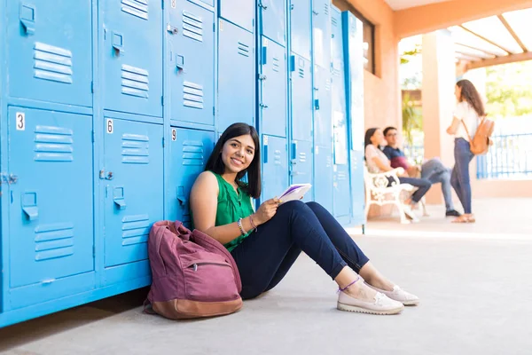 学校の廊下でバックパックに座りながら勉強している魅力的な若い女の子の肖像画 — ストック写真