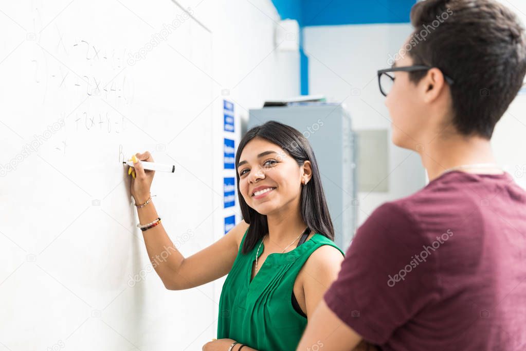 Smiling pupil writing equation on whiteboard during lecture