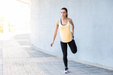 Kaldırımda dururken uzun bir koşudan önce bacağını geren kadın koşucu