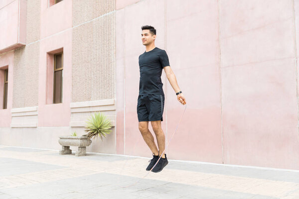 Confident male athlete exercising with jumping rope in city