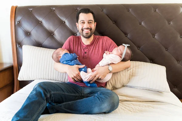 Smiling dad carrying twin babies together while resting on bed at home