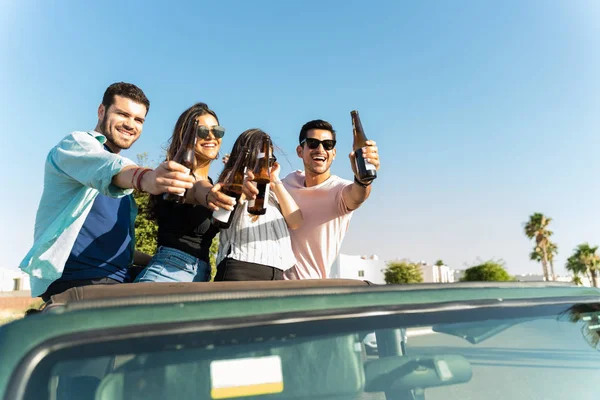 Hispanic friends toasting beer bottles while standing in SUV