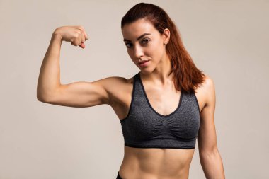 Renkli arka plan aleyhine dururken spor giyim kasları esneme genç sevimli kadın portresi